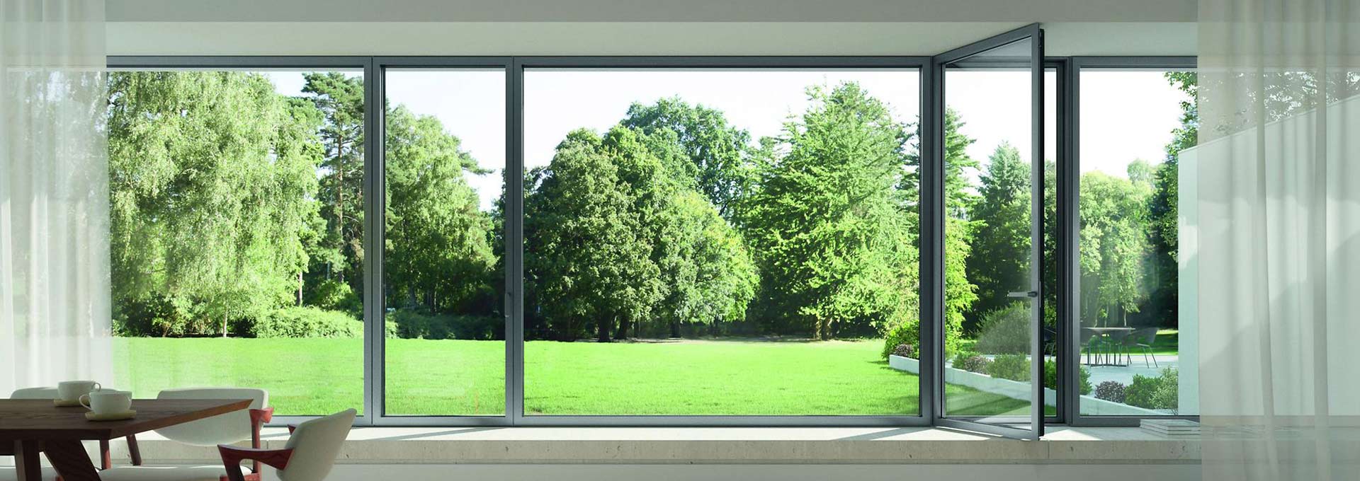 Vetrate panoramiche Schüco Roma: tecnologia e ampie superfici vetrate Vetrata panoramica Schüco in alluminio grigio antracite con sezione apribile a battente, affaccio su un ampio prato verde.