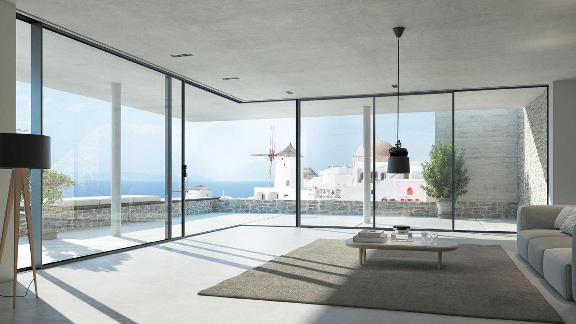 Luminoso soggiorno moderno con ampie vetrate scorrevoli panoramiche in PVC Schüco Living Slide che si affacciano su un paesaggio costiero.