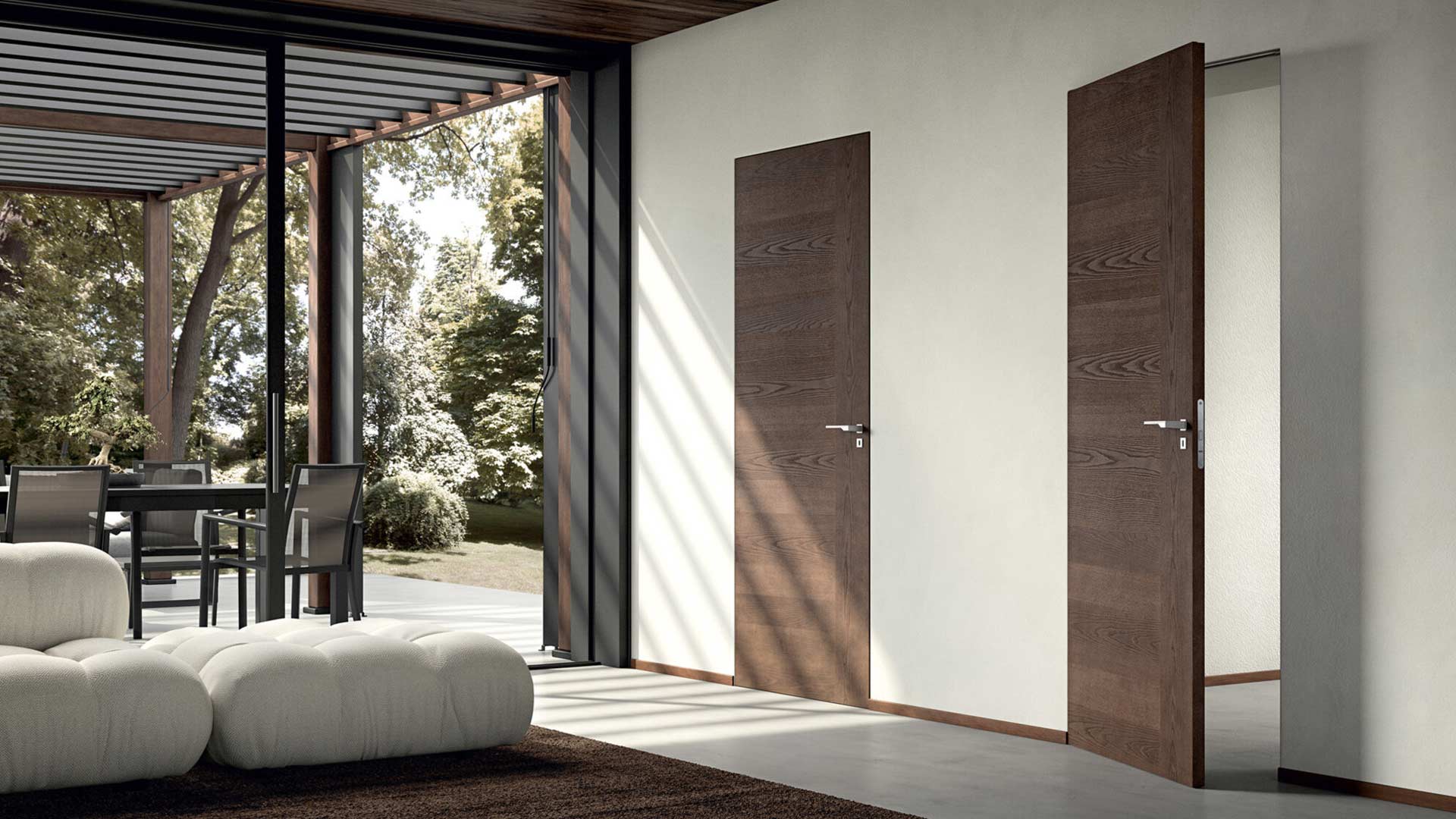 Salotto moderno con una porta filo muro laccata color tortora perfettamente integrata in una parete con boiserie in legno chiaro a listelli verticali, affiancata da un appendiabiti di design.