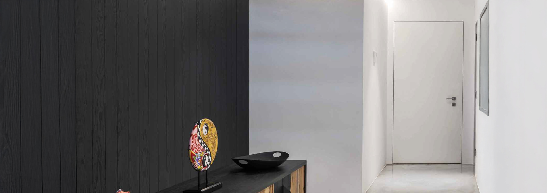 Alias rasomuro: la porta blindata che arreda i tuoi interni Porta blindata Alias da interno modello rasomuro in bianco opaco, perfettamente integrata nella parete di un corridoio dal design minimalista.