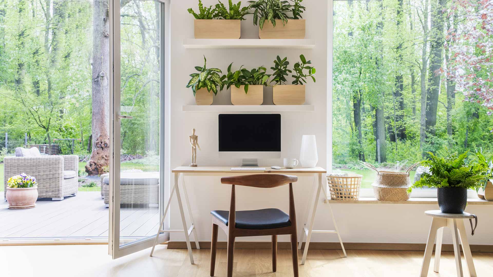 Porta-finestra moderna in PVC bianco a tutta altezza aperta su un giardino verde, all'interno di uno studio luminoso con scrivania e piante.