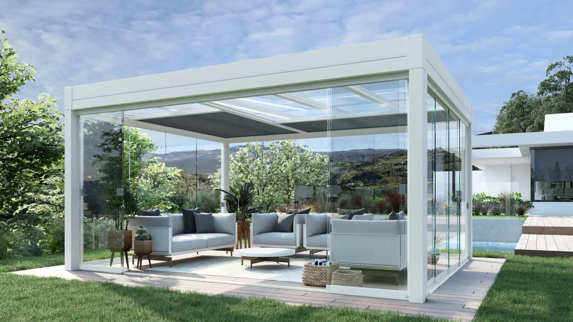 Pergola bioclimatica autoportante bianca installata in giardino. La struttura è chiusa lateralmente da vetrate scorrevoli trasparenti e arredata come un elegante salotto moderno.