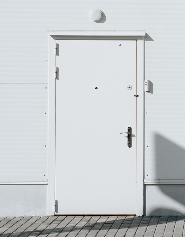 Dettaglio di una robusta porta tagliafuoco tecnica laccata bianca e perfettamente chiusa, installata su una parete industriale con illuminazione a plafone.