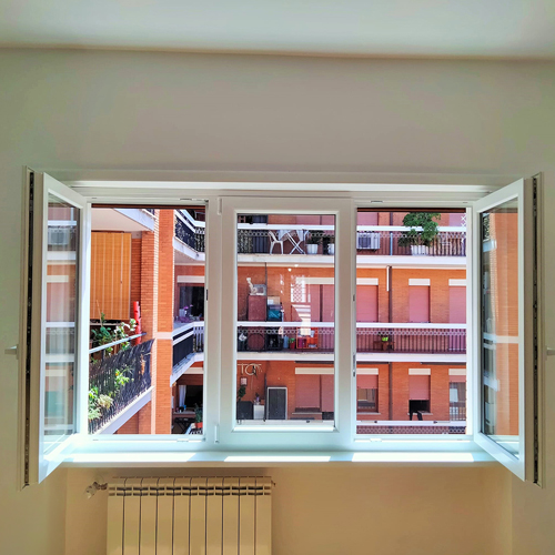 Finestra in PVC bianco a tre ante aperta su un cortile residenziale a Roma