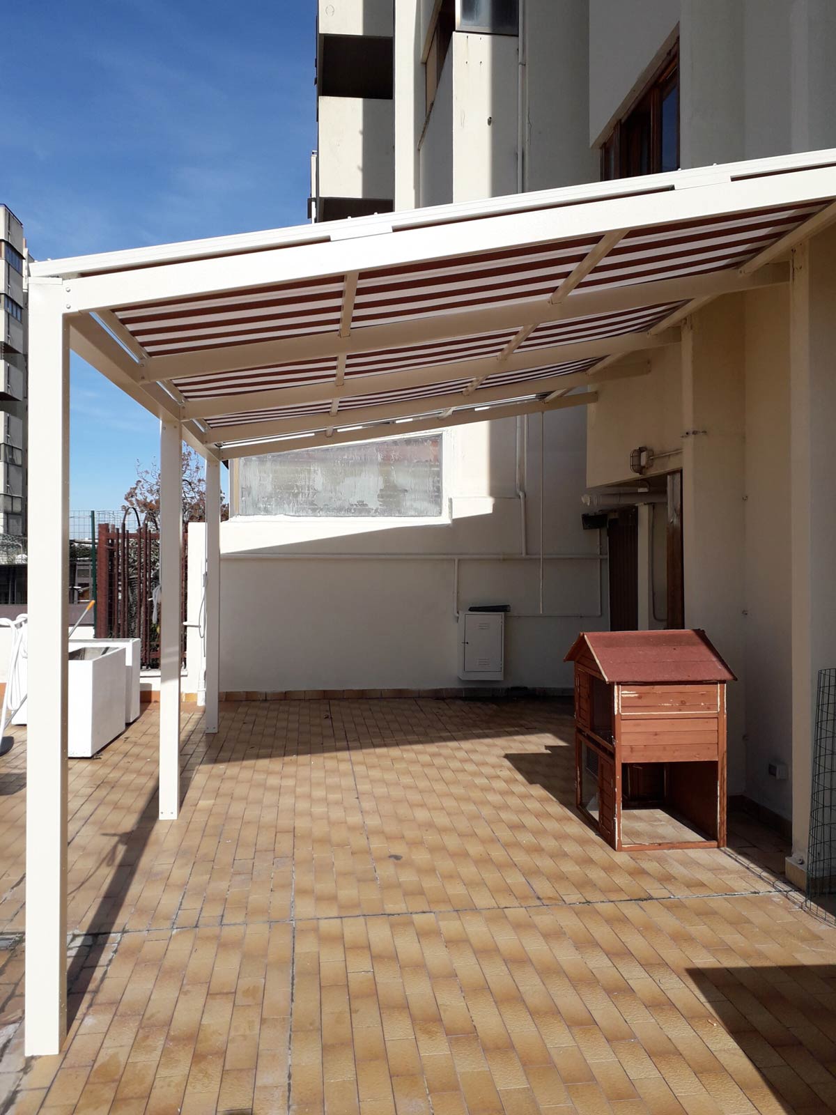 Struttura pergotenda con telo a righe retraibile installata su un terrazzo piastrellato