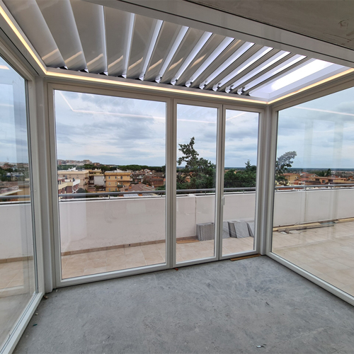 Interno di una pergola bioclimatica bianca con lame frangisole e vetrate scorrevoli su un attico a Roma