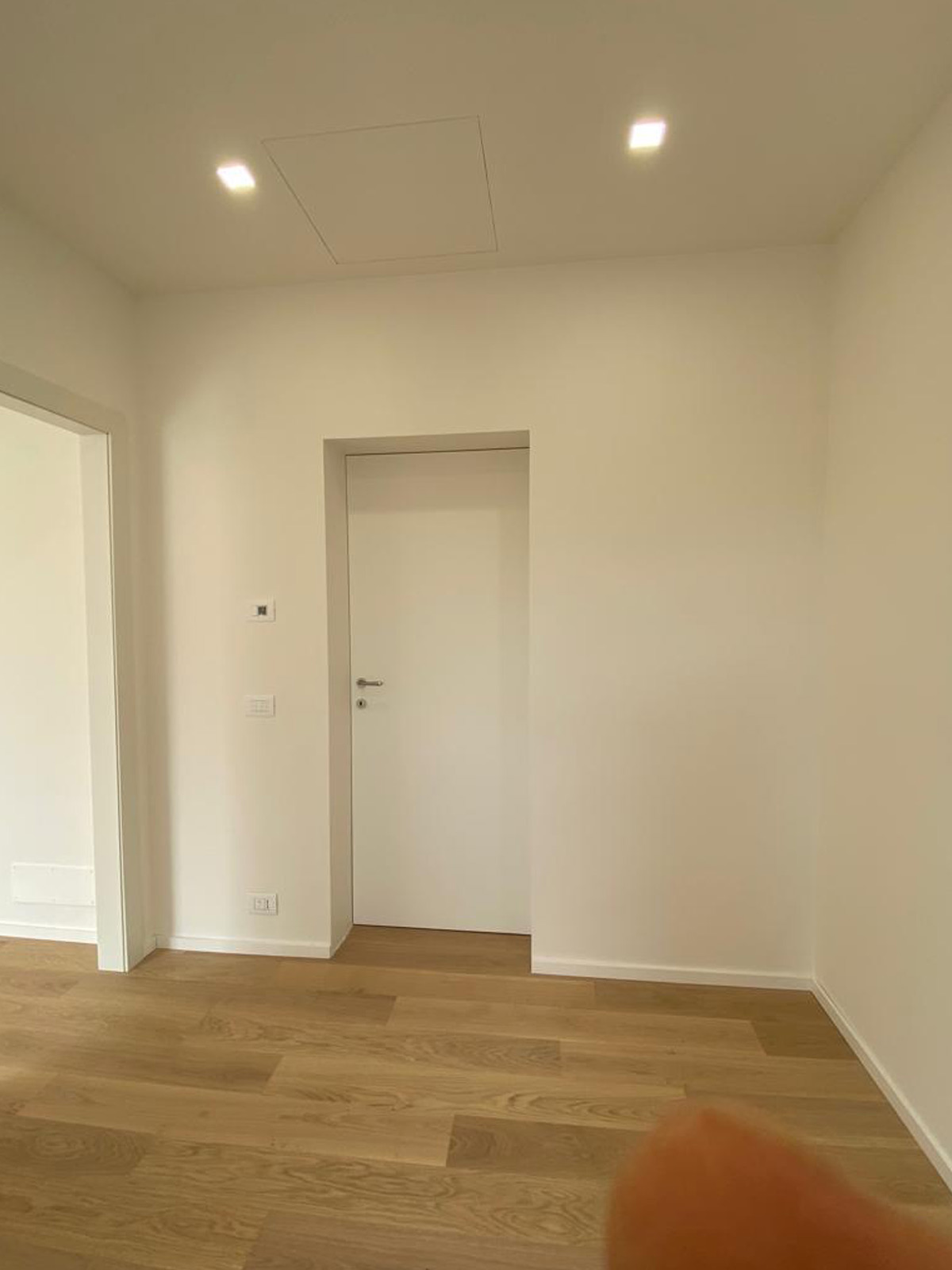 Porta interna bianca filomuro installata su parete bianca in una stanza con parquet in rovere