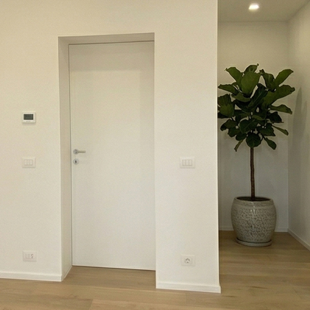 Elegante ingresso di una villa all'Olgiata con porta filomuro bianca DoorArreda e pianta decorativa