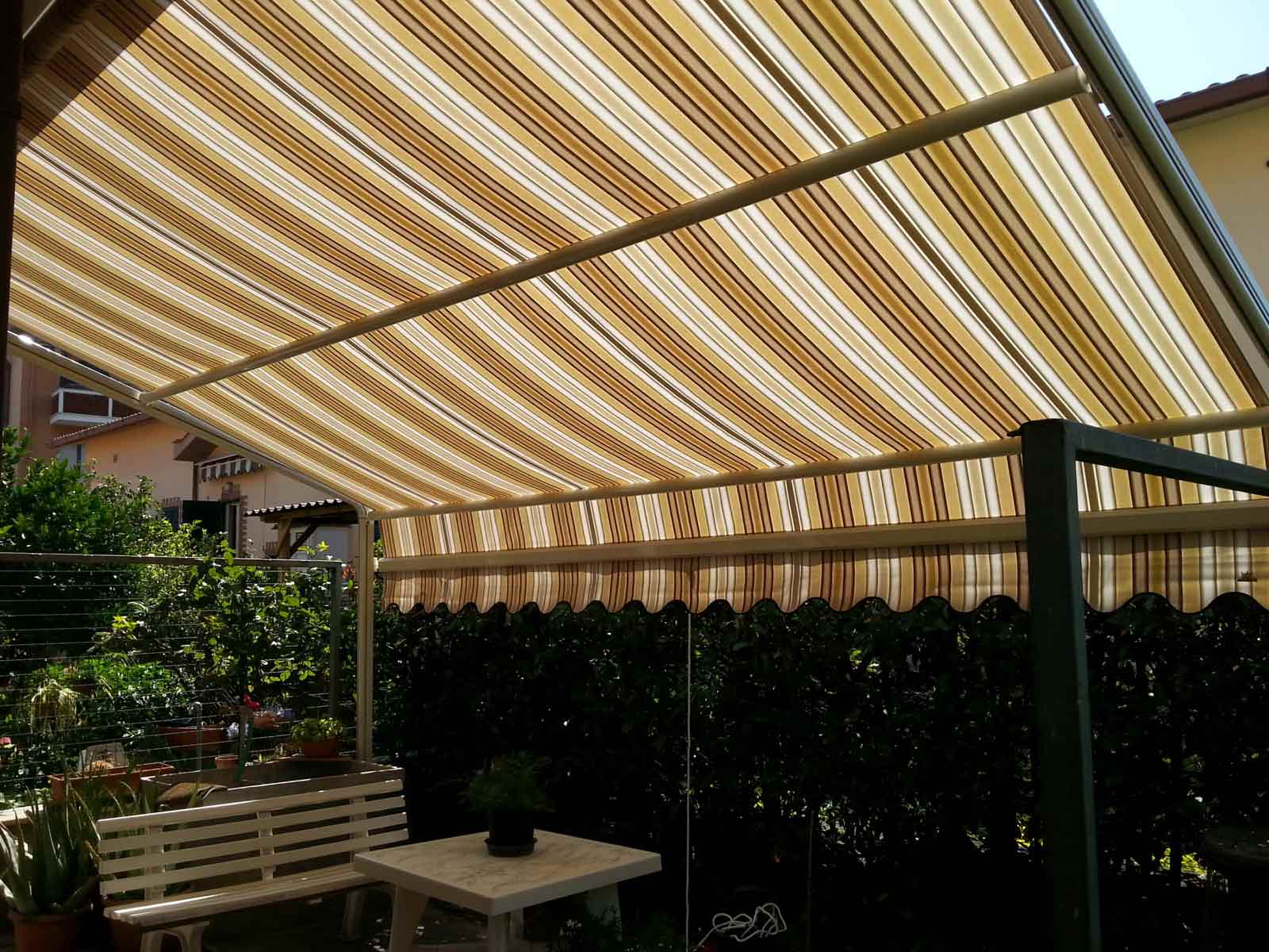 Tenda da sole a bracci estensibili con tessuto a righe beige e marroni installata in un giardino
