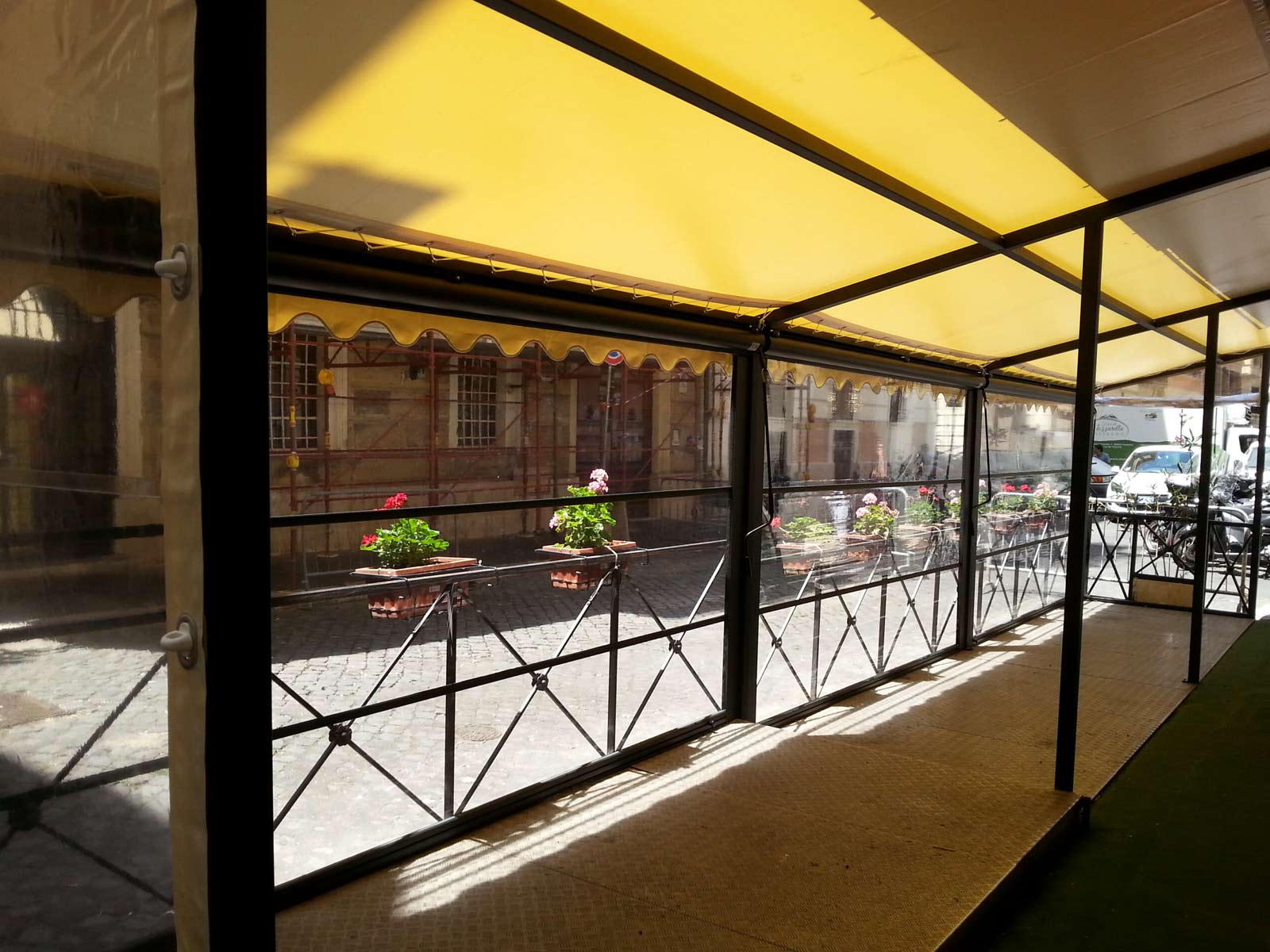 Tenda da sole gialla abbinata a chiusure laterali in PVC trasparente per proteggere un plateatico esterno