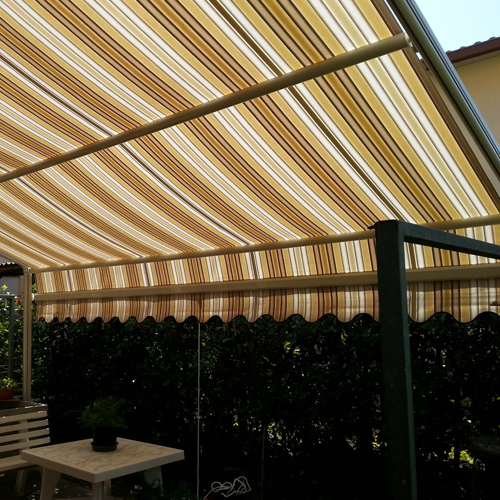 Tenda da sole a bracci estensibili con tessuto a righe beige e marroni installata in un giardino