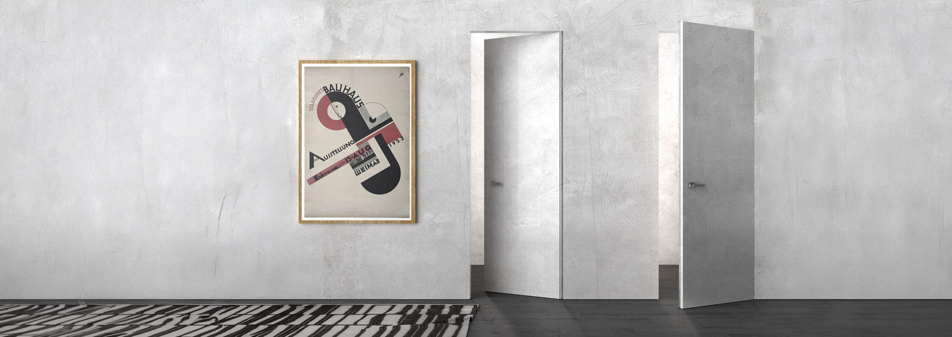 Agoprofil Filomuro: porte d'arredo minimaliste e moderne Coppia di porte filomuro Agoprofil perfettamente integrate in una parete materica grigio cemento con poster artistico Bauhaus.