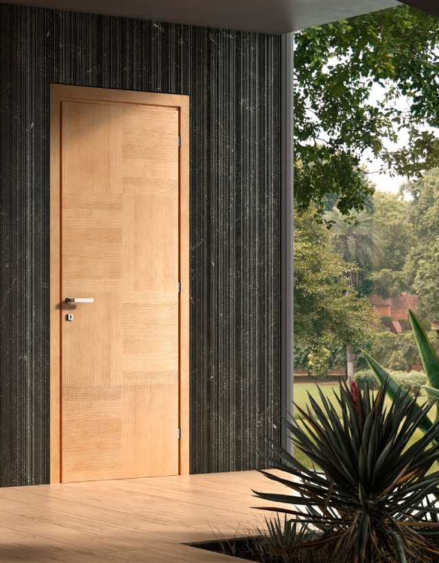 Dettaglio di una porta d'interno a battente GD Dorigo con finitura materica in legno chiaro, installata in un ambiente dal design scuro ed elegante che si affaccia su un giardino.