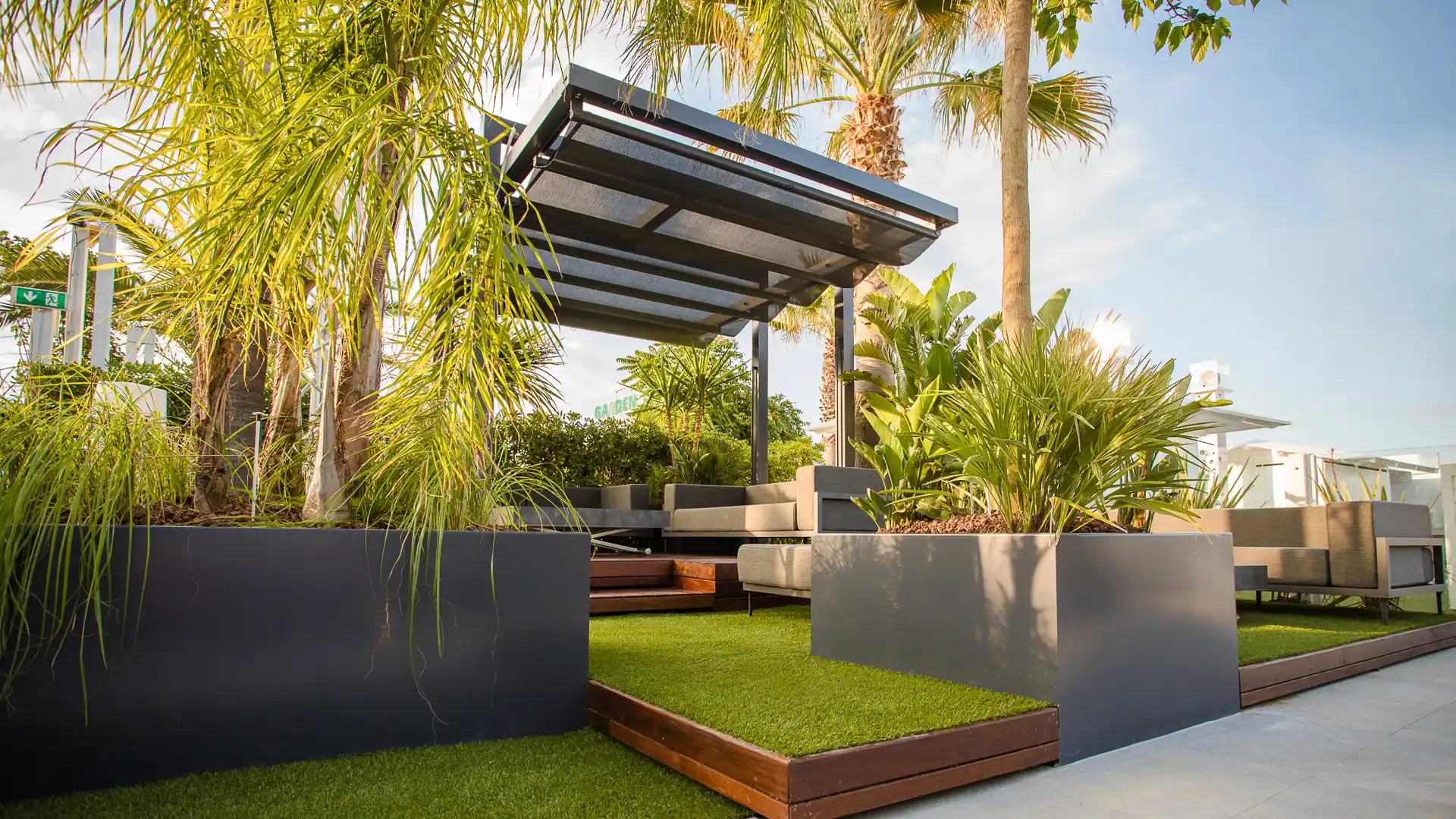Moderna pergola in alluminio Giulio Barbieri con tetto scorrevole, installata in un elegante terrazzo lounge con piante decorative.