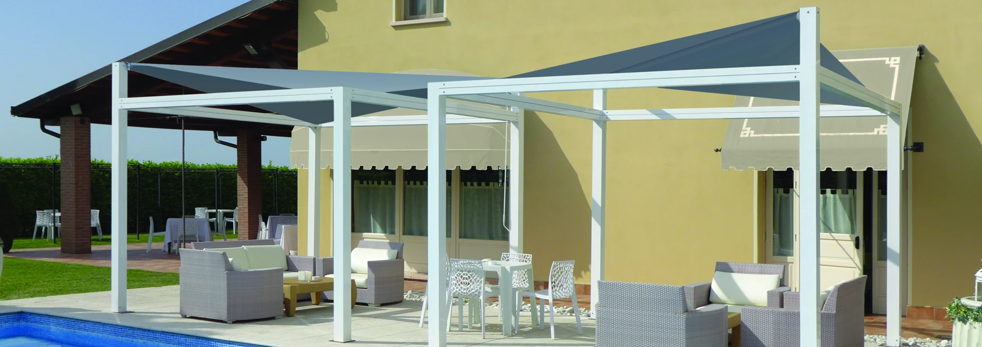 Vele ombreggianti Giulio Barbieri: design nautico e linee minimaliste per esterni di lusso. Struttura autoportante bianca Giulio Barbieri con vela ombreggiante tesa di colore scuro, che ripara una zona lounge a bordo piscina.