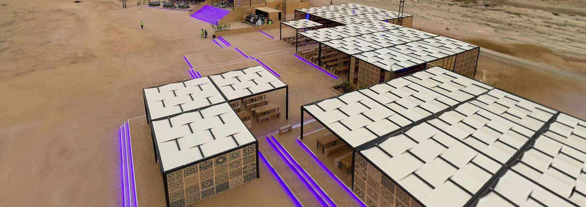 Coperture modulari Giulio Barbieri: soluzioni outdoor su misura per grandi spazi ed eventi. Installazione modulare di ampie pergole Giulio Barbieri con copertura a telo intrecciato chiaro, posizionate su un'estesa area sabbiosa con luci LED.