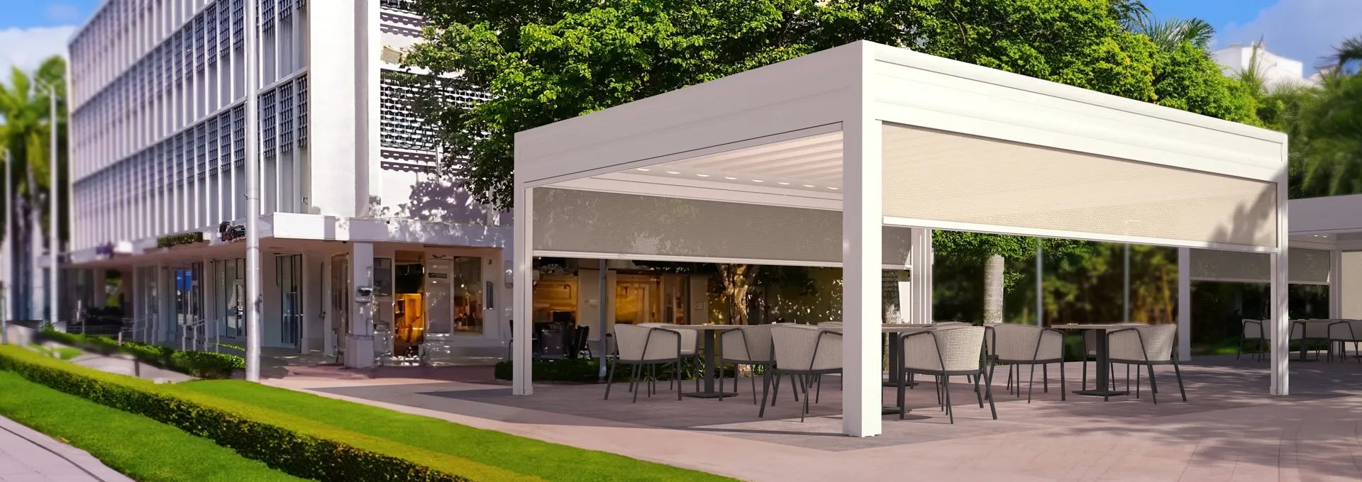 Pergole Giulio Barbieri con chiusure laterali: vivi l'outdoor urbano in totale privacy. Elegante pergola autoportante bianca Giulio Barbieri con tende verticali a caduta integrate, a copertura dei tavoli di un bar in contesto urbano.